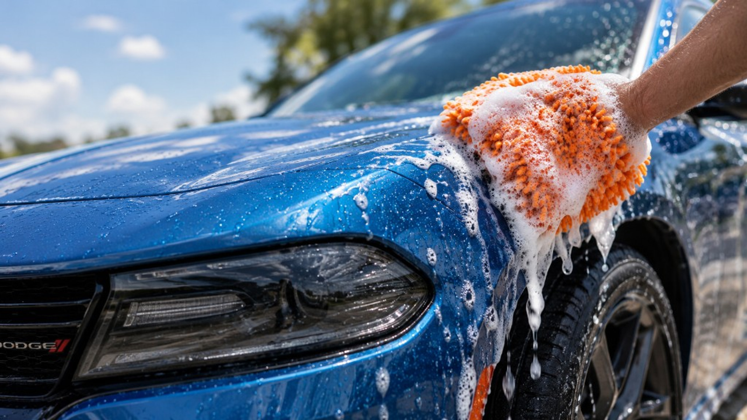 Orange wash mitt and suds on a blue car during a Prime Wash hand wash
